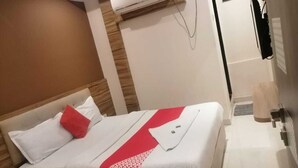 A hotel room with a bed, a bedside table, an air conditioning unit, and a small bathroom area. - HOTEL RUBY (Mumbai)