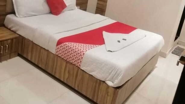 A neatly made bed with a red pillow, a white blanket, and a red and white patterned throw. - HOTEL RUBY (Mumbai)
