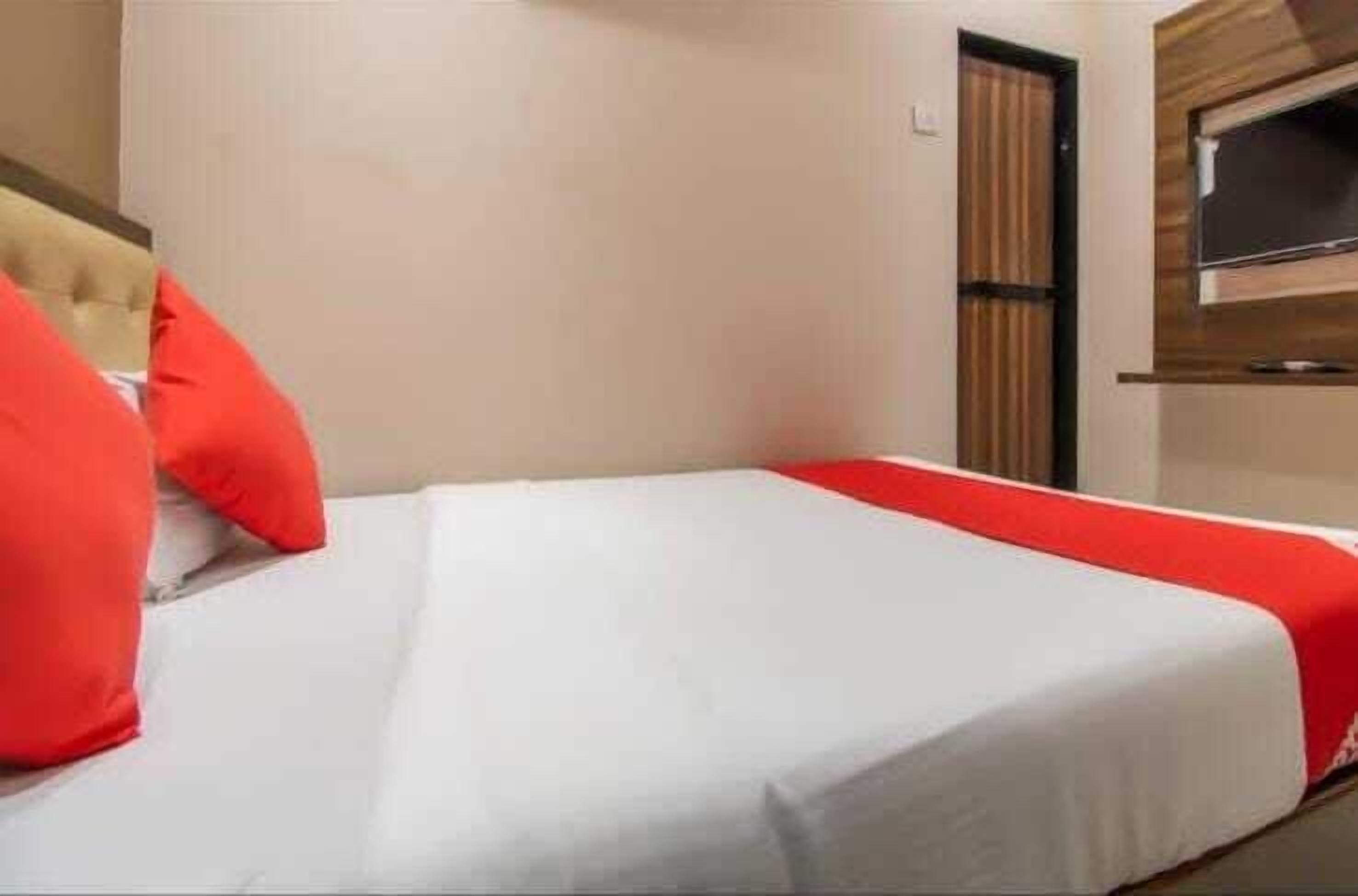 A hotel room with a bed, a TV mounted on the wall, and a wooden door.