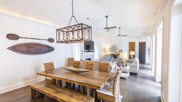 A spacious dining area with a wooden table and benches, surrounded by wicker chairs. - Starfish Cottage & Carriage House | Large Property with Private Pool (Rosemary Beach)