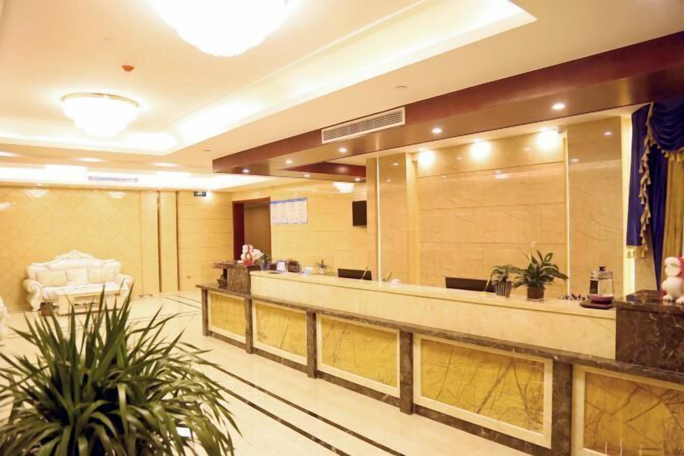 A hotel reception area with a marble counter, a white sofa, and a large potted plant.
