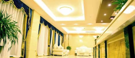 A hotel lobby with a polished floor, a reception desk, and a seating area with sofas.