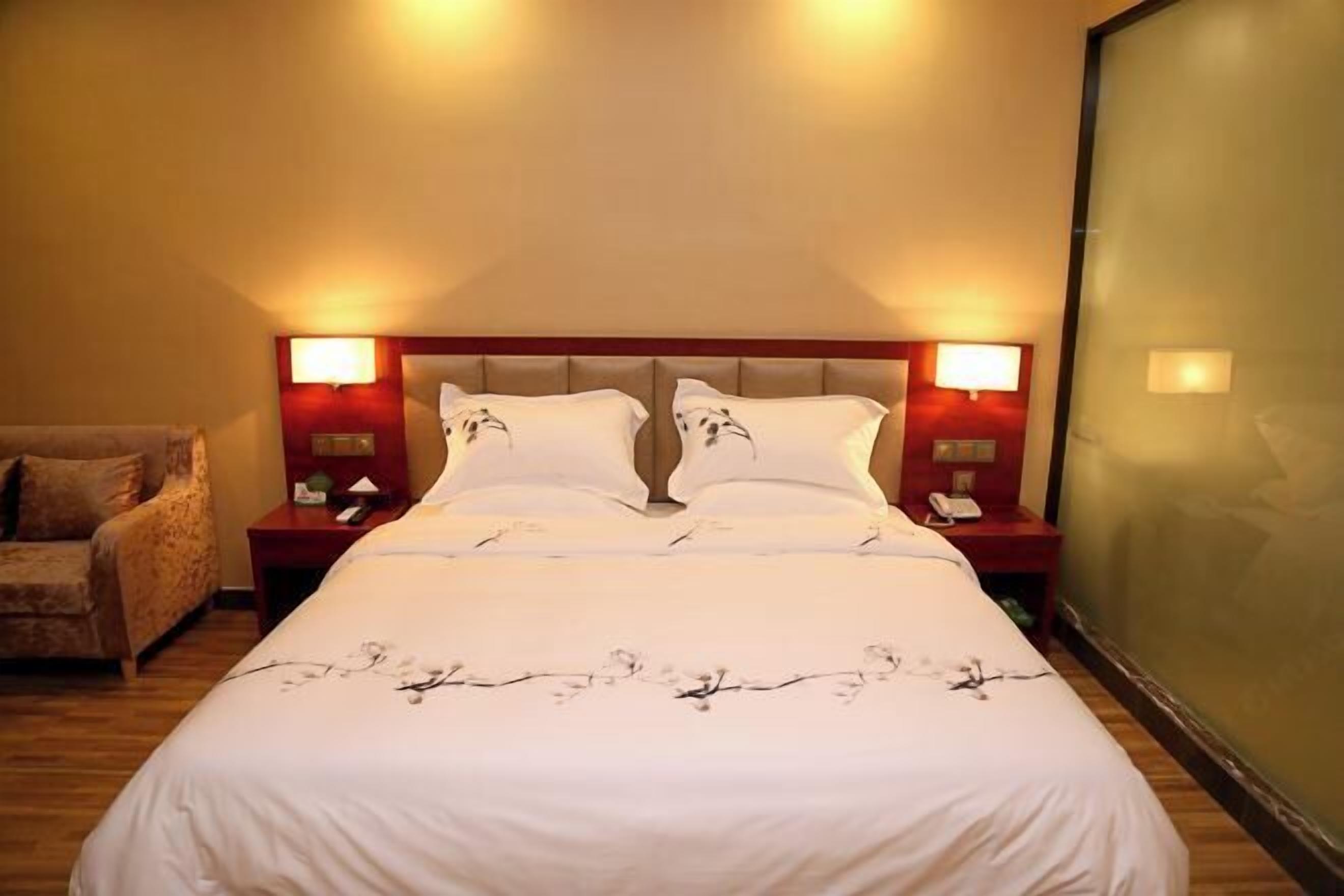 Een hotelkamer met een groot bed, twee nachtkastjes met lampen, een stoel en een groot raam.