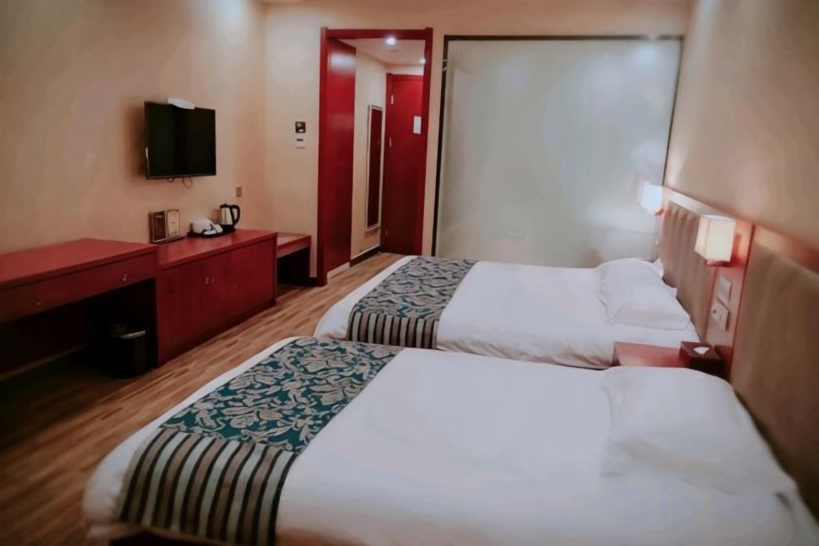 A hotel room with two beds, a desk, a TV, and a door leading to another room.