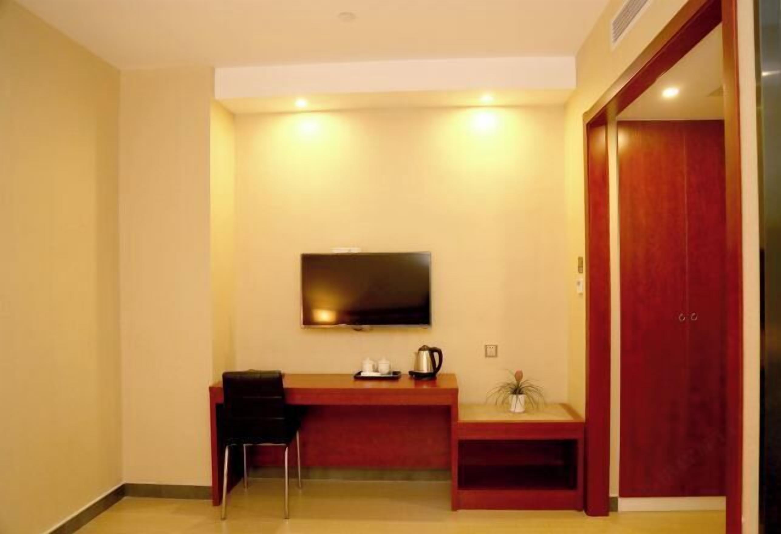 Habitación de hotel con escritorio de madera, televisor de pantalla plana en la pared, una pequeña zona de estar y un armario rojo.