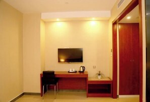 A hotel room with a wooden desk, a flat-screen TV mounted on the wall, a small seating area, and a red wardrobe. - Ruju Business Hotel (Wuhu)