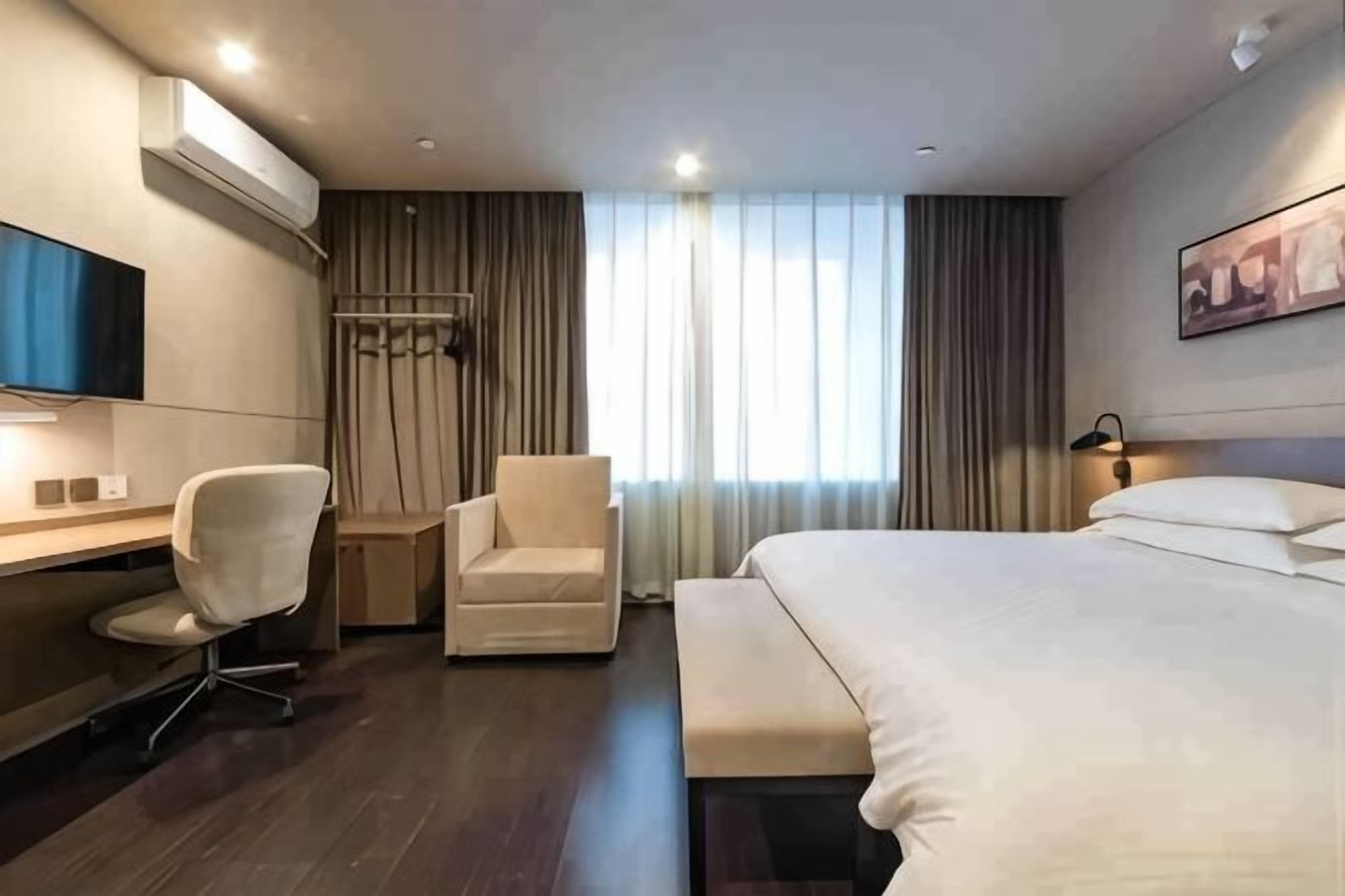 A hotel room with a bed, a desk, a chair, a TV, and a window with curtains.