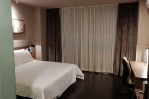 Habitación de hotel con cama, escritorio, silla, mesita de noche y ventana con cortinas.