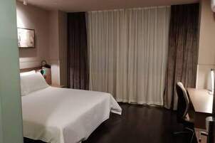 Habitación de hotel con cama, escritorio, silla, mesita de noche y ventana con cortinas.