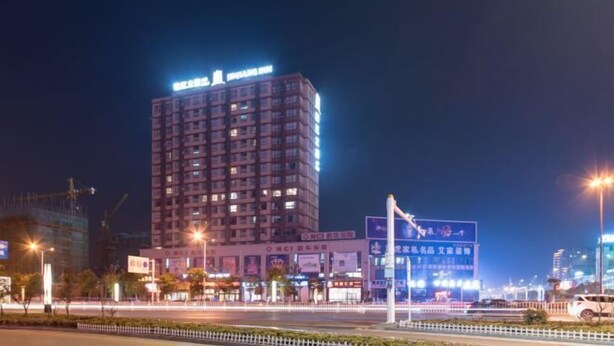 Um hotel com vários andares, com sinalização iluminada, uma rua bem iluminada e edifícios comerciais ao redor.