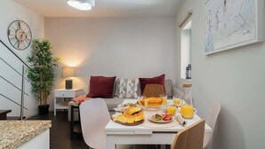 A modern dining area with a table set for breakfast, a sofa with cushions, a potted plant, and a wall clock. - Central Duplex Porto House by HostWise (Porto)