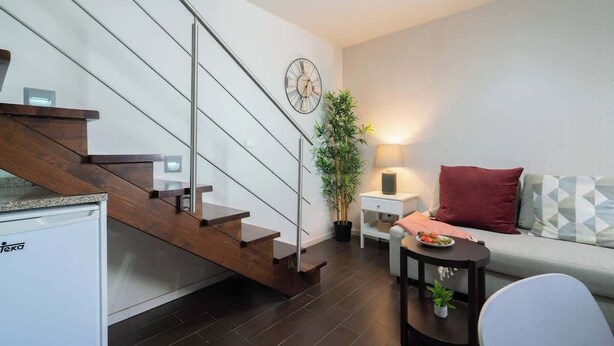 A modern living room with a staircase, a sofa, a side table, and a small plant. - Central Duplex Porto House by HostWise (Porto)
