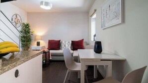 A modern living room with a sofa, a dining table, and a kitchen area with a clock and a plant. - Central Duplex Porto House by HostWise (Porto)