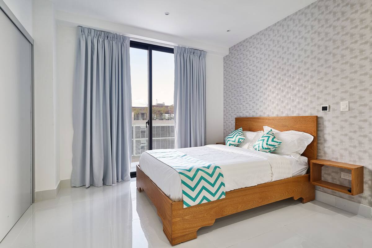 A modern bedroom with a wooden bed, grey curtains, and a patterned wallpaper.
