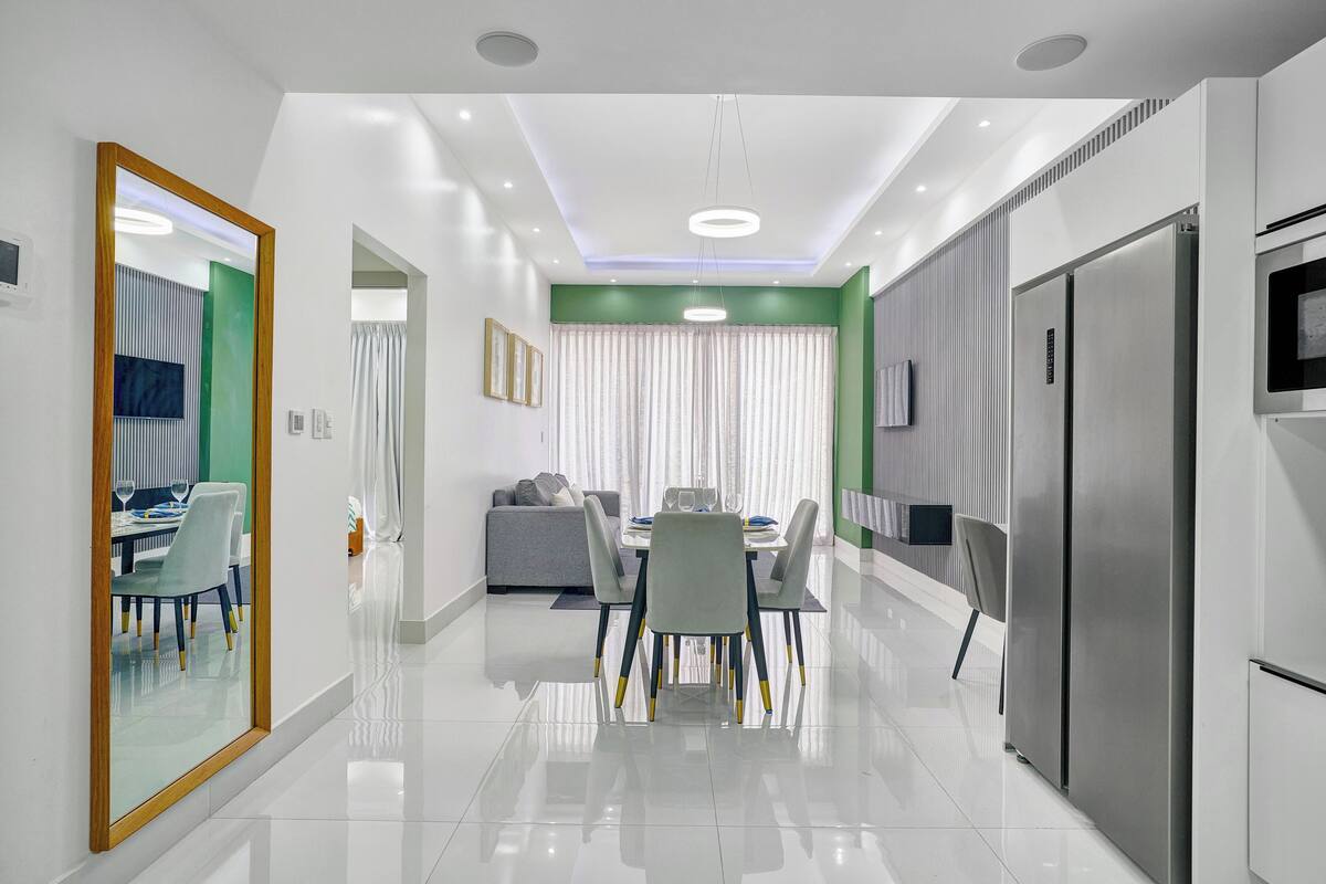 A modern kitchen with a stainless steel refrigerator, a dining area with a table and chairs, and a living area with a sofa.