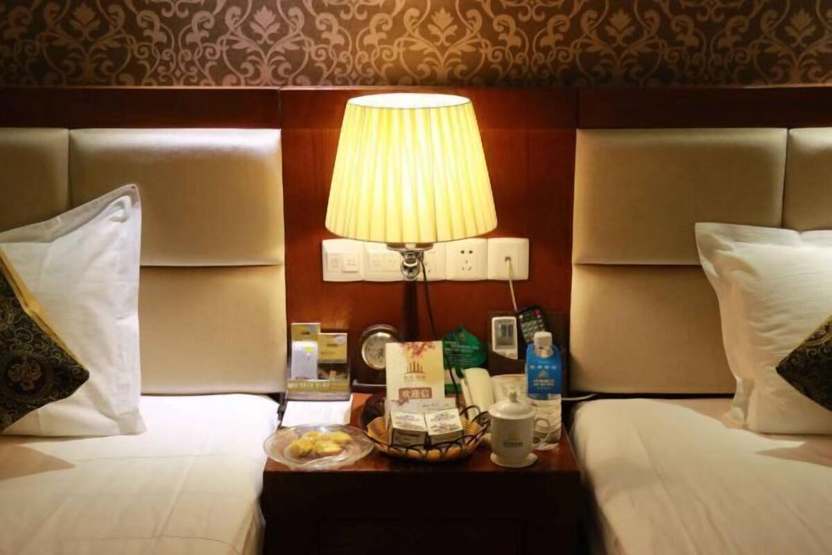A hotel room with a bed, a nightstand with a lamp, a tray with snacks, and a small table with toiletries.