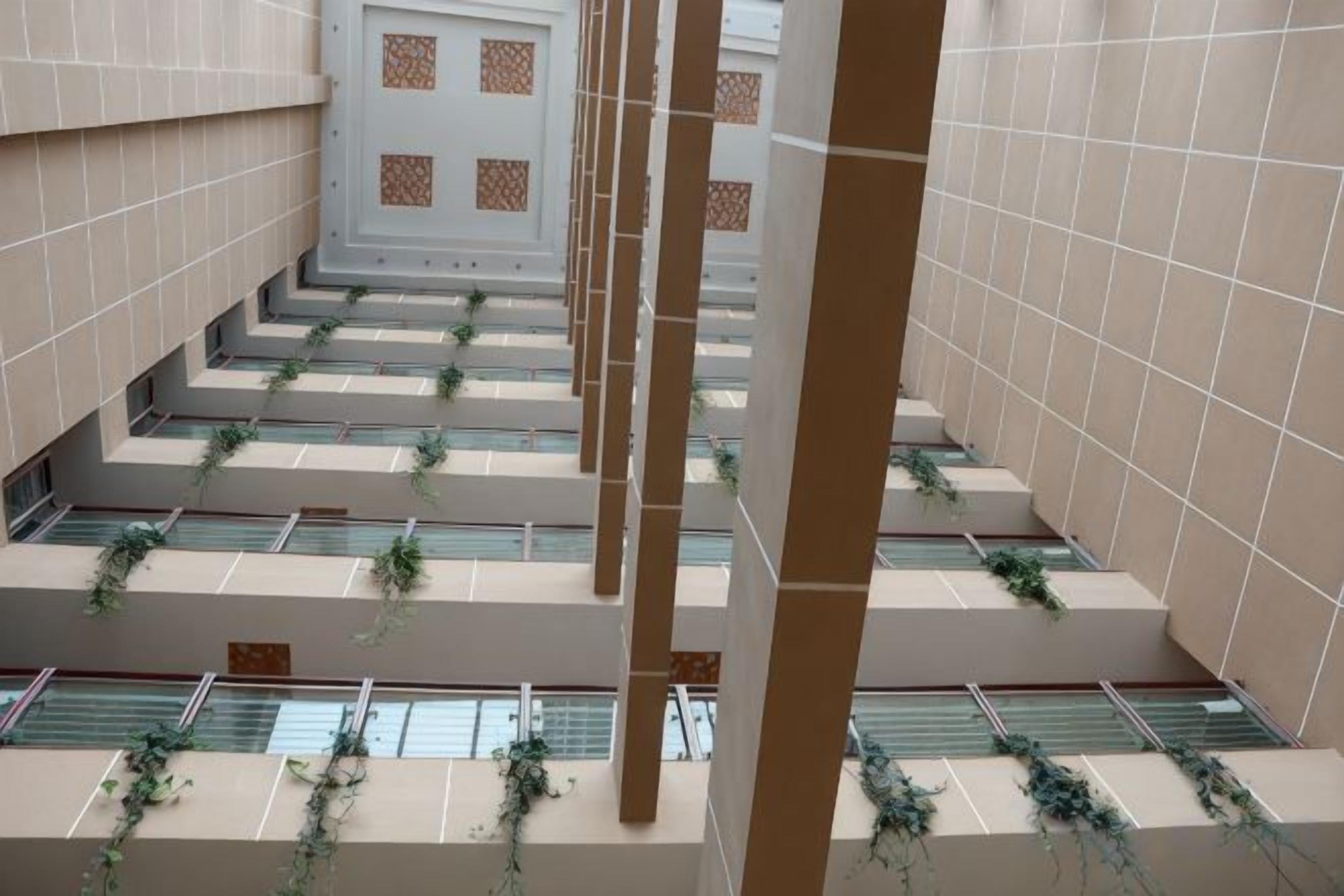 Ein mehrgeschossiges Interieur mit gefliesten Wänden, einer zentralen Treppe und Bepflanzung auf den Stufen.