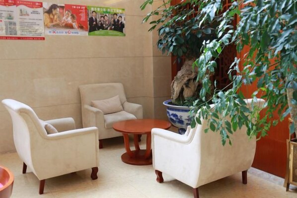 Un vestíbulo con tres sillones blancos, una mesita redonda y una planta grande en maceta.