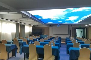 Un salón de conferencias con mesas y sillas, una pantalla de proyector y una pantalla grande mostrando un cielo con nubes.