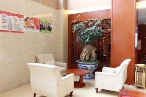 A lobby with two white armchairs, a wooden coffee table, a large potted plant, and a traditional Chinese-style screen. - Qingtian Boutique Hotel (Zhaotong Fengxia Road) (Zhaotong)