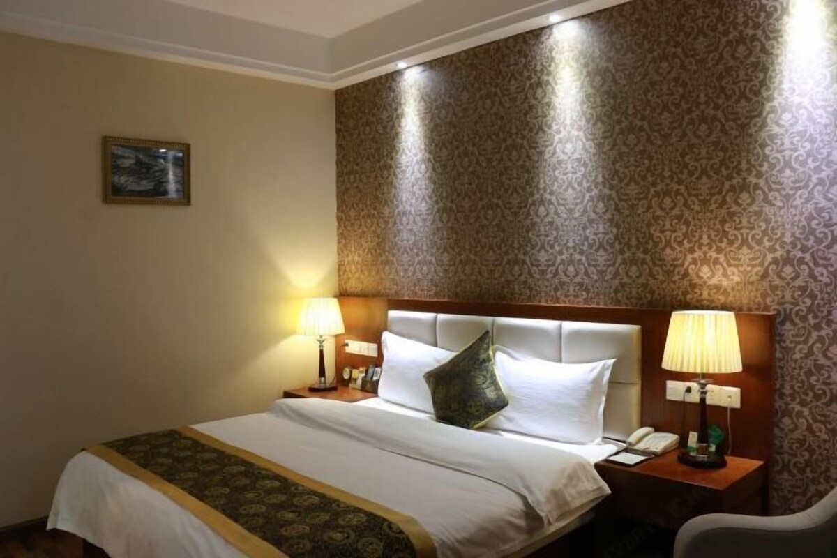 A hotel room with a large bed, two bedside lamps, a nightstand, and a chair.