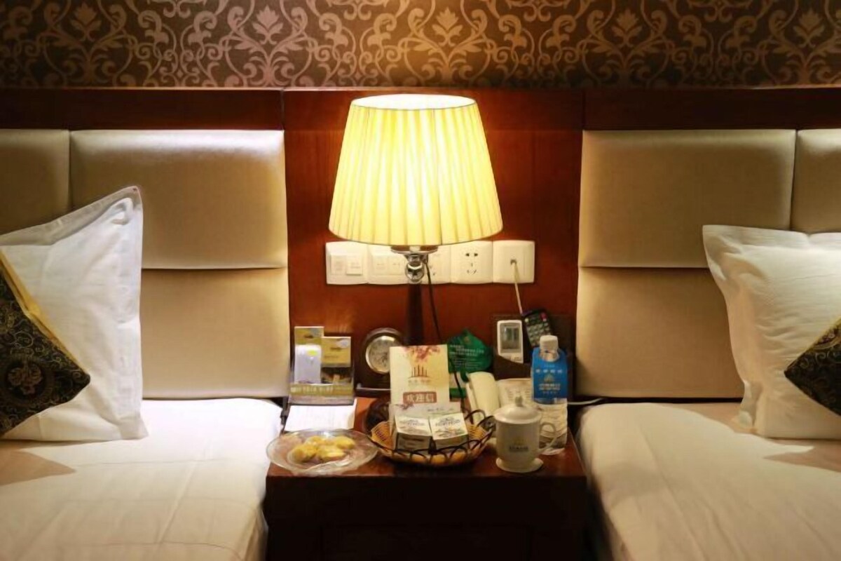 A hotel room with a bed, a bedside table with a lamp, a clock, and various toiletries.