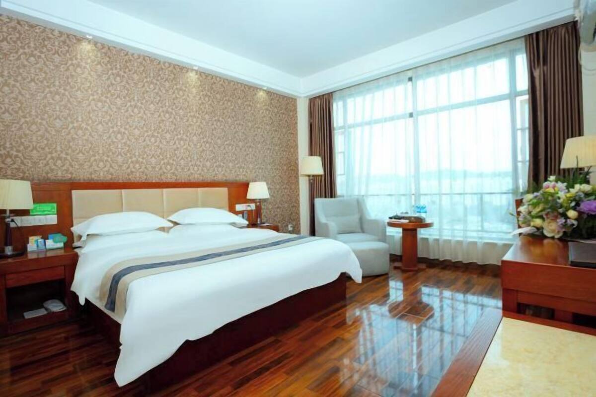 A hotel room with a large bed, a chair, a desk, a lamp, and a window with curtains.
