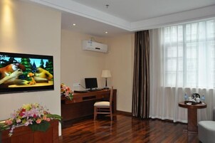 A hotel room with a wooden desk, a chair, a television, and a large window with curtains.