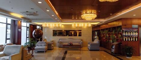 A hotel lobby with a chandelier, sofas, a reception desk, and a wall with framed pictures.