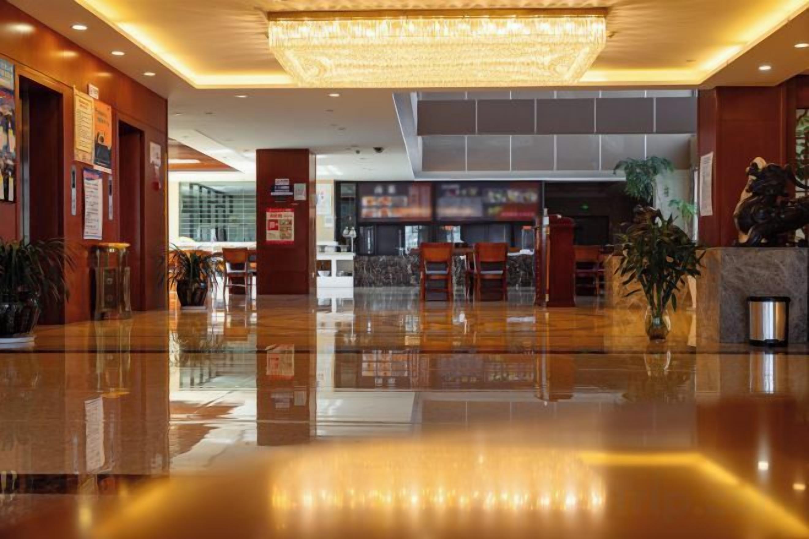 A hotel lobby with a reflective floor, a large chandelier, and a reception desk.