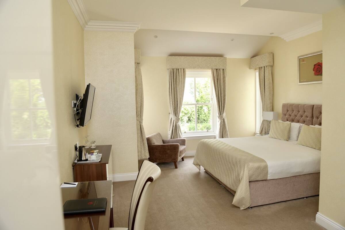 A hotel room with a large bed, a desk with a chair, a television, and a window with curtains.