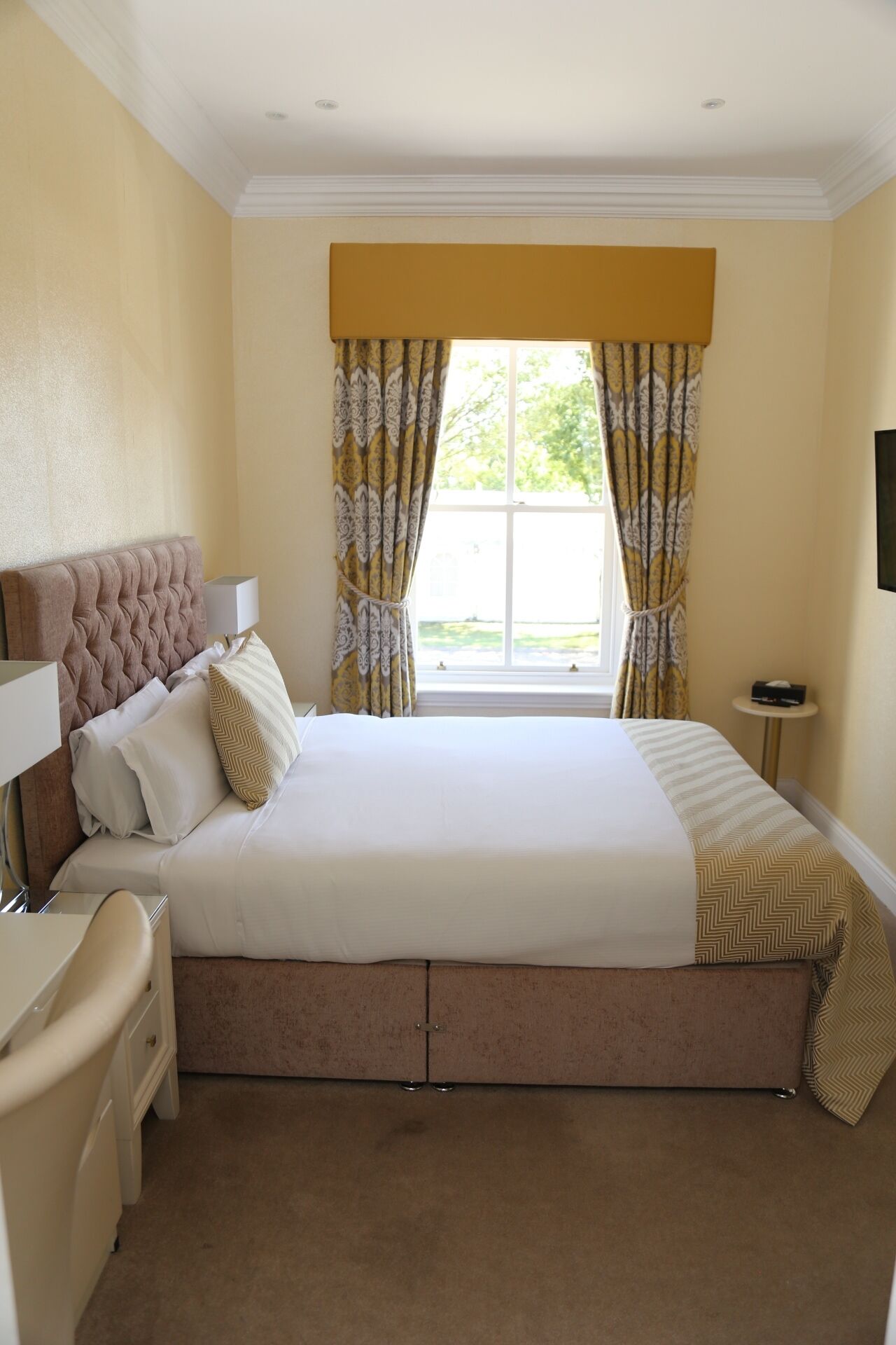 A hotel room with a large bed, a bedside table, a chair, and a window with curtains.