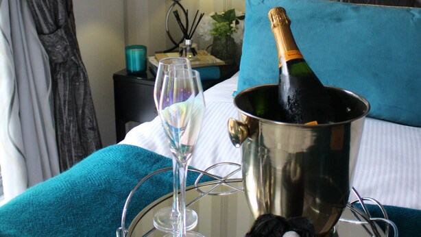 A bed with a champagne bottle, a glass, and a tray. - The Old Hall Hotel (Coventry)