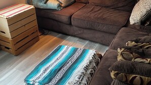 Ein gemütliches Wohnzimmer mit einem braunen Sofa, gemusterten Kissen, einer Holzbank und einer gestreiften Decke.