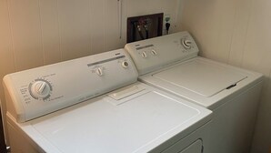 Eine Waschmaschine mit Frontlader und ein Trockner befinden sich in einem Waschraum, über dem Trockner ist ein Fenster.