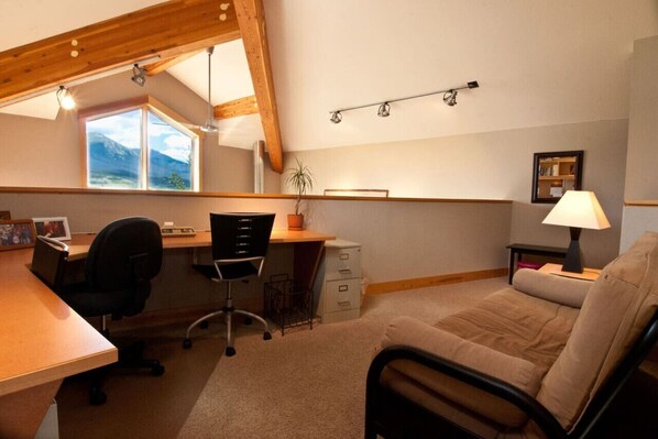 Une pièce comprenant un bureau, un fauteuil de bureau et un canapé. Il y a une fenêtre donnant sur les montagnes.