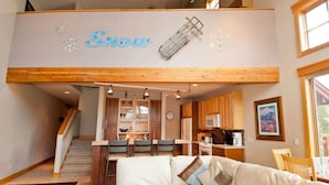 A cozy interior with a living area, kitchen, and dining space. A sign with snowflakes and the word "Snow" is visible. - Mountain-View Condo in Dillon • Walk to Dining & Lake • Close to Keystone (Dillon)