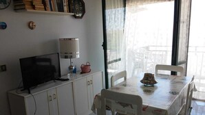 A dining area with a table covered in a tablecloth, chairs, a television, a lamp, and a basket on a cabinet.