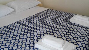 A hotel room with a bed, white pillows, a patterned bedspread, and two towels on the bed.