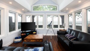 A living room with a large TV, a wooden coffee table, a black leather sofa, and a telescope.