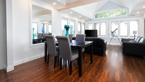A spacious living room with a dining area, large windows, and a high ceiling.
