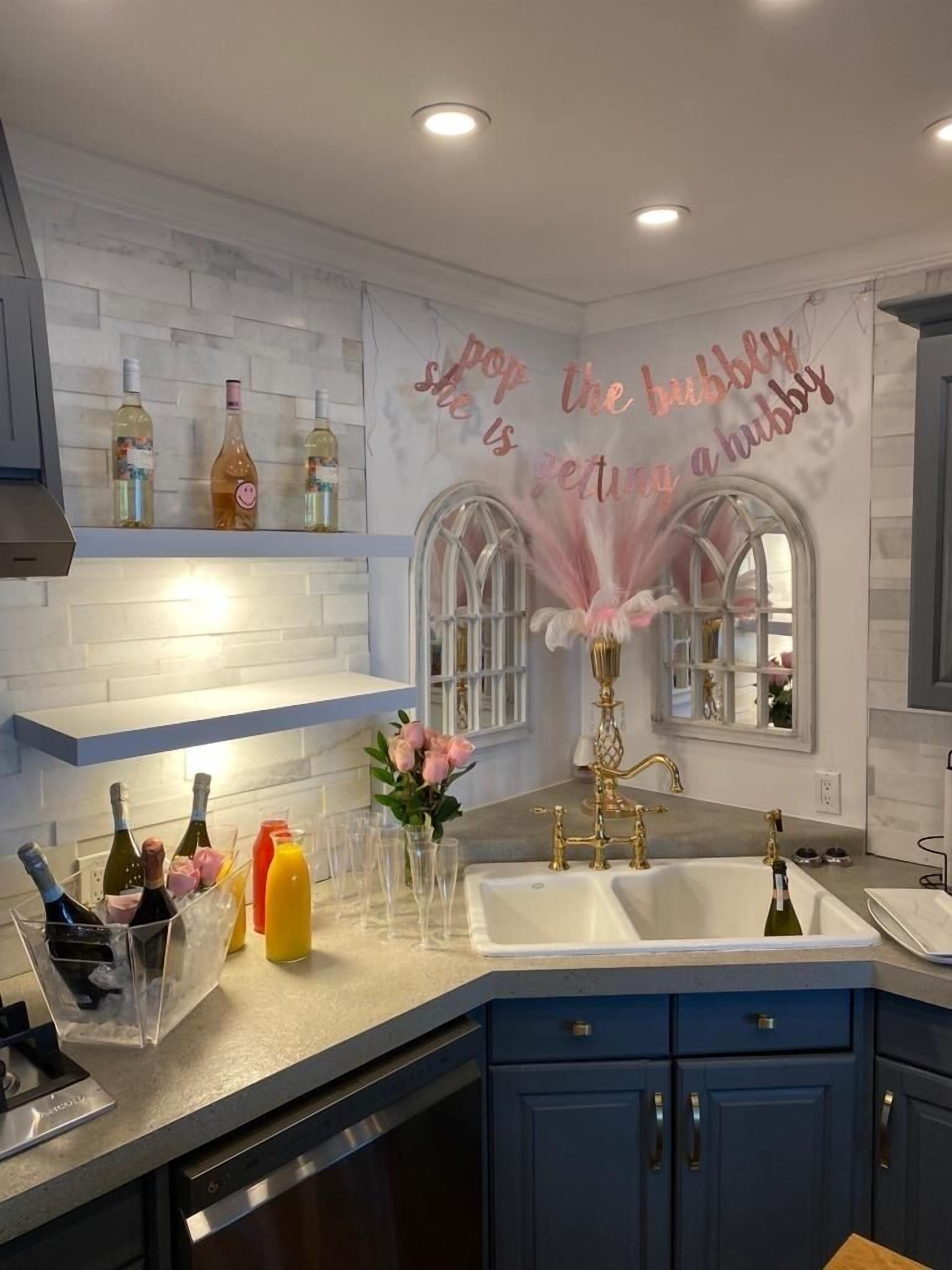 Une cuisine avec un mur recouvert de carreaux blancs, des armoires bleues, une fenêtre décorative et un mur orné d’une inscription.