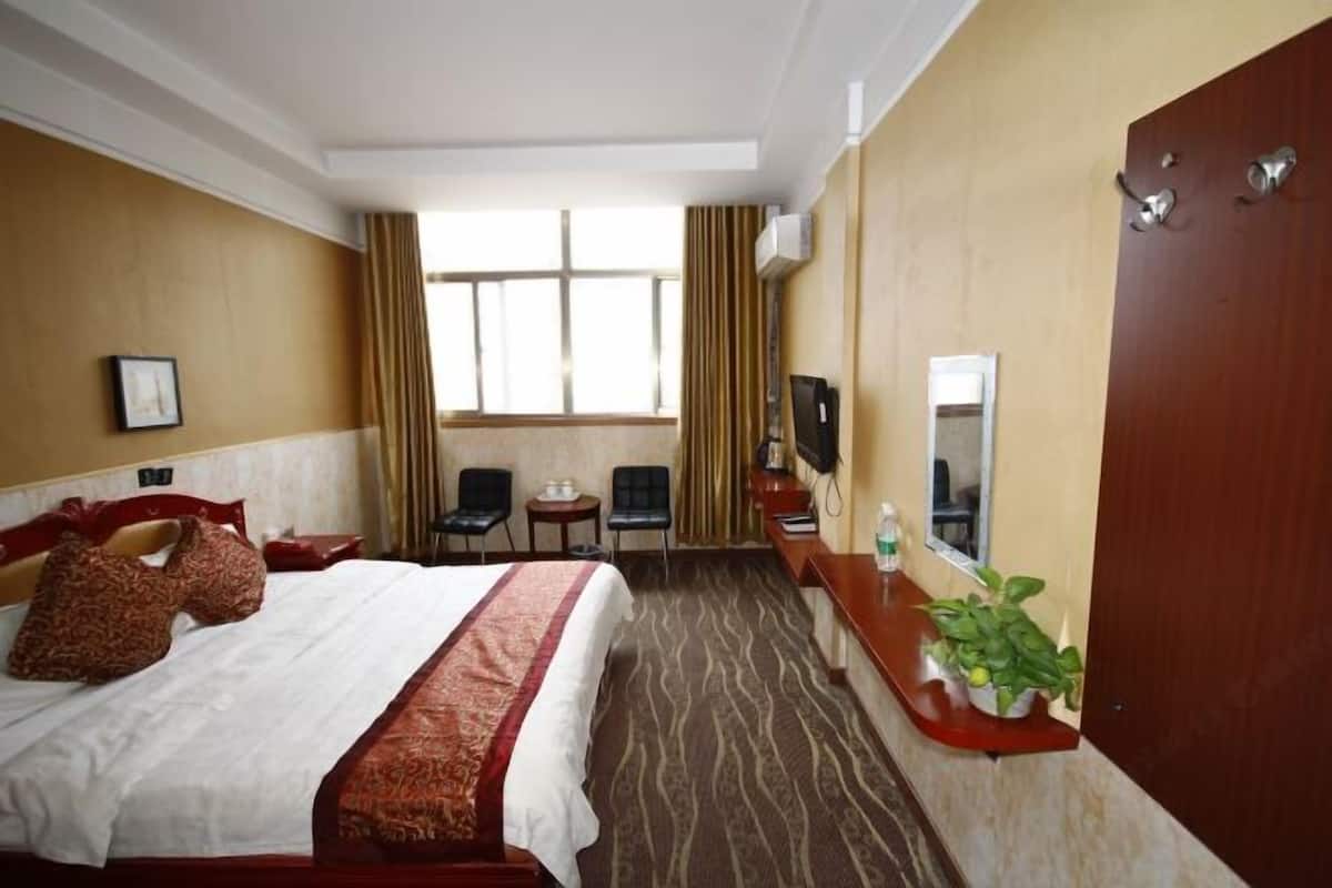 Ett hotellrum med en säng, ett skrivbord med en stol, en tv, ett fönster med gardiner och en dörr.