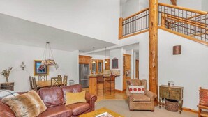 A spacious living area with a brown leather sofa, a wooden coffee table, and a staircase with a wooden railing. - Elegant, sleep 8, private hot tub, gourmet kitchen (Sunriver)
