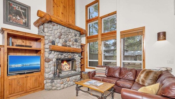 A cozy living room with a stone fireplace, leather sofa, and a television on a wooden cabinet. - Elegant, sleep 8, private hot tub, gourmet kitchen (Sunriver)
