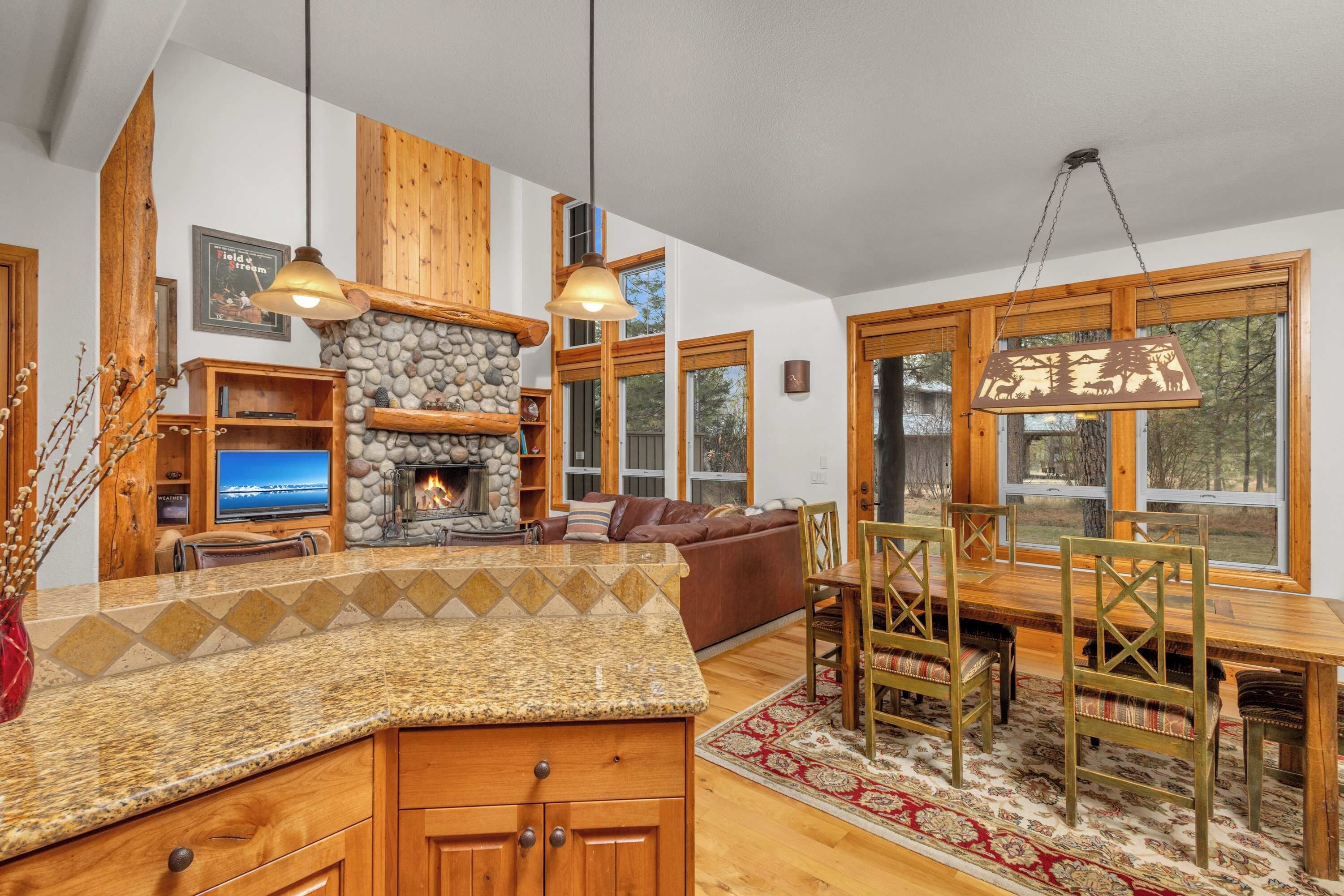 A cozy living room with a stone fireplace, wooden furniture, and large windows.