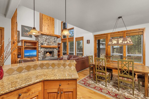 A cozy living room with a stone fireplace, wooden furniture, and large windows.