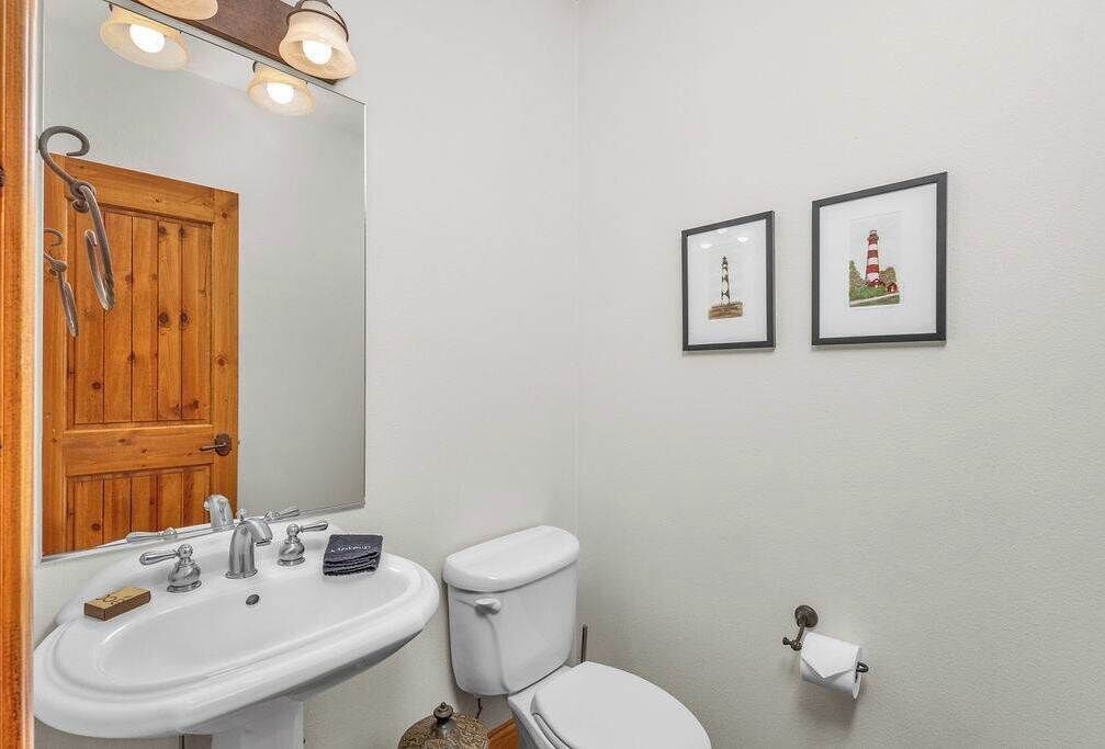 Un baño con puerta de madera, un lavamanos blanco, un inodoro y dos cuadros en la pared.