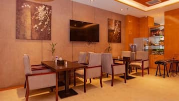 A hotel room with a dining area, a flat-screen TV mounted on the wall, and a minibar.