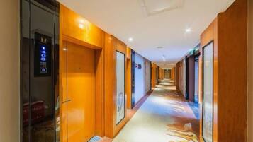 A hotel corridor with doors on both sides, a patterned carpet, and a ceiling light fixture.